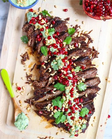 Pomegranate brisket with avocado cilantro aioli laying on a wooden board on a table.