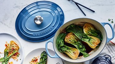 oval le creuset in blue with cooked vegetables inside