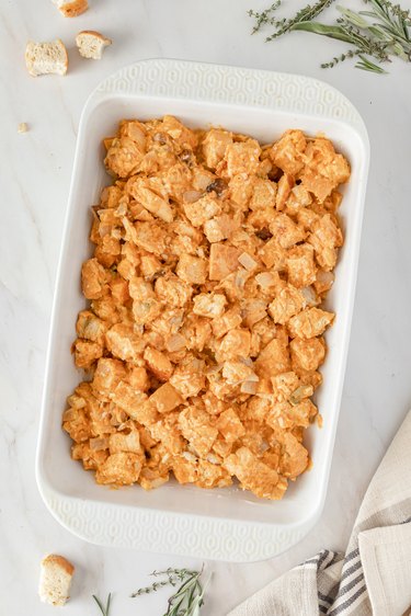 A white casserole dish filled with the squash and bread mixture on a white marble countertop.