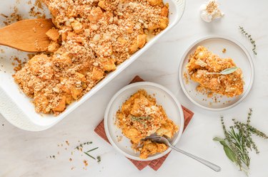 The squash bake in a white casserole dish next to two small white plates with pieces of the bake on them.