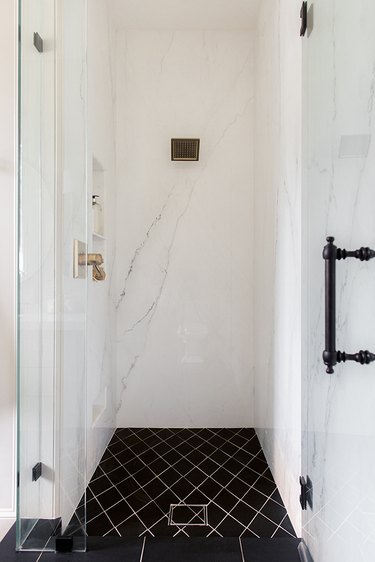 MInimalist walk-in shower with marble tile and black fixtures.