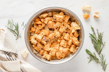 The bread and liquid mixtures combined in a silver metal bowl on a white marble countertop.