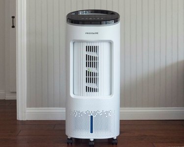 Portable black and white evaporative cooler in room with pale gray wall, white woodwork, dark wood or laminate flooring