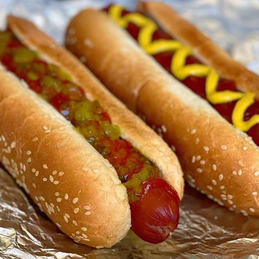 Close up of two hot dogs, one with ketchup and relish and the other with mustard.