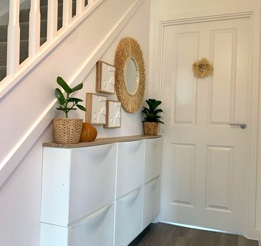 A white Trones IKEA shoe cabinet in a short hallway topped with plant pots.
