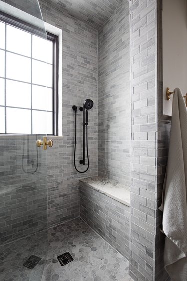 Gray and white marble walk-in shower with black and gold hardware.