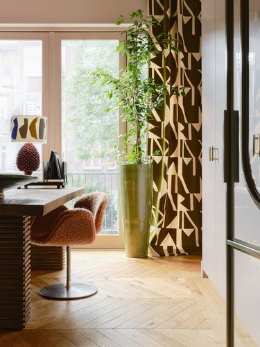 An office in browns and whites is accented by a graphic print patterned curtain.