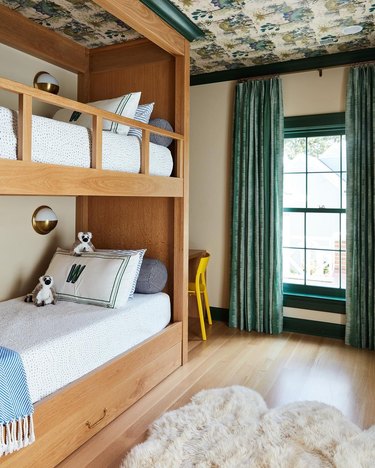 Children's bunkbed room with teal curtains and wallpapered ceiling.