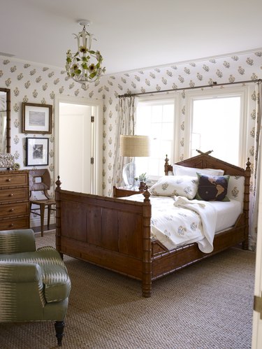 A bedroom with dark wood bed frame and orange and white block print floral wallpaper and curtains
