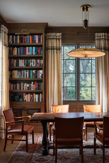 Dark wood and leather study with beige curtains.