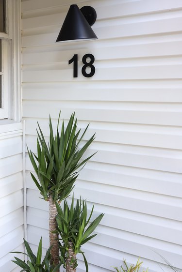 Black cone wall sconce and black floating street numbers next to plant
