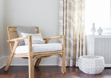 A light rattan chair with white and gray cushions is paired with a marble patterned curtain.