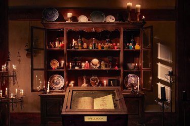 Winifred Sanderson's spell book in a case in front of wooden shelf lined with potions and candles.