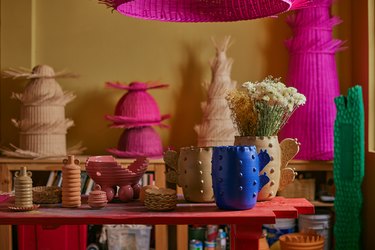 Mestiz original mugs and art pieces on a red table in front of a pale yellow wall.