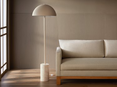 A floor lamp with a travertine stone base and a mushroom-shaped beige shade next to a grey sofa.