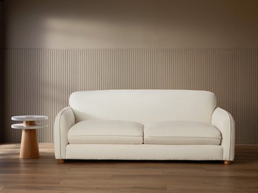 A white pillowy sofa next to a side table made of wood and marble.
