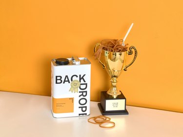 Backdrop paint can next to a gold trophy in front of an orange wall.