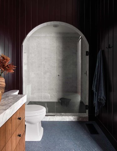 Bathroom with black shiplap walls, arched shower. Gray penny tile floors.