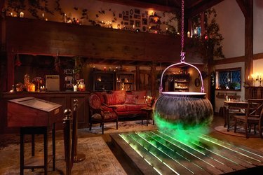 Interior of the Hocus Pocus Cottage with an ancient red couch, glowing green cauldron, and candles lining the room.