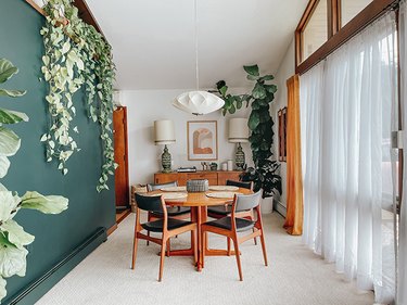 A living room with green walls, lots of plants, and double layered window treatments