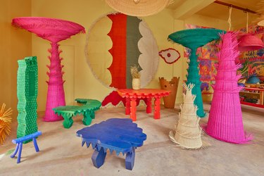 Mestiz original furniture designs in green, bright pink, blue, and orange in front of a yellow wall.