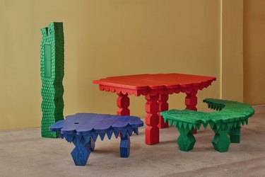 Mestiz furniture designs in red, blue, and green in front of a pale yellow wall.