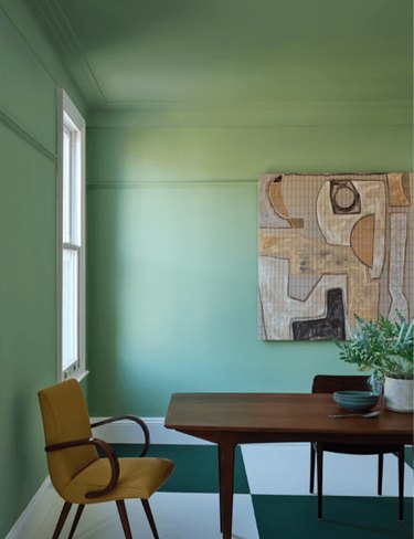 Farrow & Ball's bright green paint color on the wall behind a wood dining table and yellow upholstered dining chair.