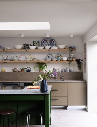 Farrow & Ball beige paint color on a kitchen wall behind open wood shelving covering in various plates and bowls.