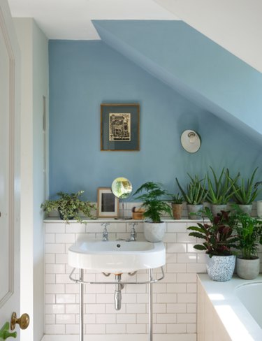 Farrow & Ball's light blue paint color on a bathroom wall that has white tile on the bottom half and a white sink.