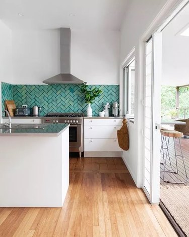 Kitchen with stainless steel gray appliances and work surfaces, white cabinets and teal backsplash