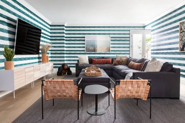 Teal and white stripe walled living room with gray sofa and beige wicker chairs