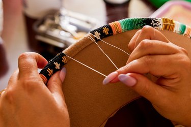 Hands weaving colored string onto a brown hat.