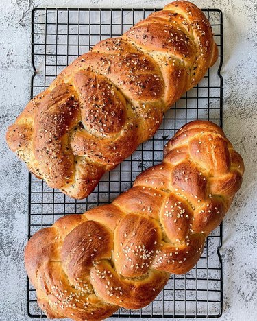Two loaves of vegan challah topped with sesame seeds on a cooling rack.