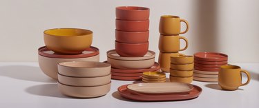 Various plates, bowls, platters, and mugs in saffron (red-orange), coriander (blush-beige), and turmeric (dark yellow) colors.