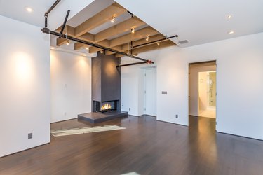 Accent wood beams in a ceiling over a fireplace in a room with dark wood flooring