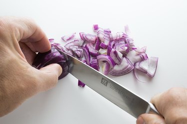 Hands cutting a red onion with a large knife