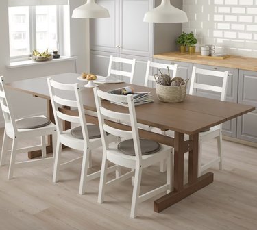 Iamge of a brown Nordic style dining table with six white chairs around it.