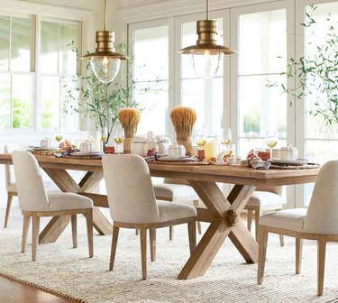 Image of large light wood farmhouse table with x-shaped legs. The table is set and ready for a meal.