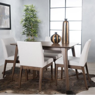 Image of a Scandinavian style dining table in dark walnut with four chairs around it. There are two striped vases on the table and plant in the corner.