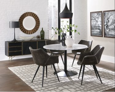Image of a round dining table with four leather chairs around it. The table has a white marble top and a black pedestal base.