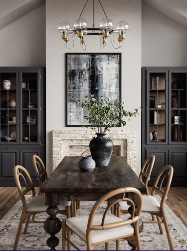 Image of large farmhouse dining table in a farmhouse dining room. There are black vases on the table and five chairs are visible around the table.