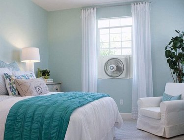 Reversible white fan installed in window of aqua and white bedroom