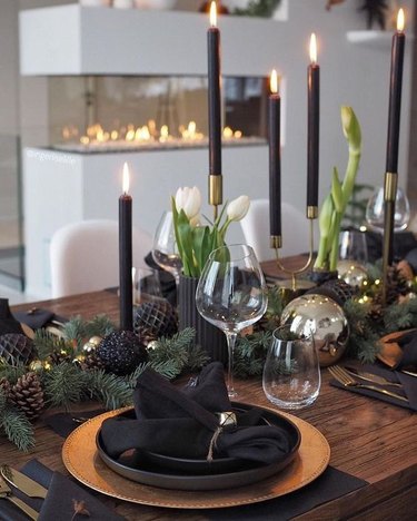 Table setting with black plates, candlesticks, and dark pinecones and golden placemats and candlestick holder