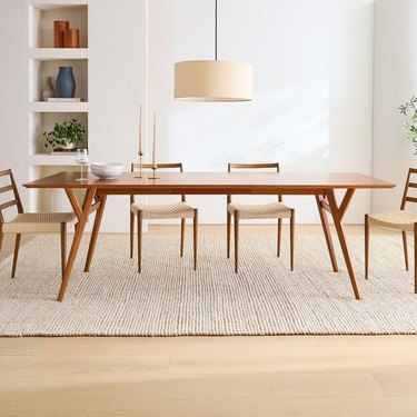 Image of a large wood Scandi-style table surround by chairs in a sparsely decorated room.