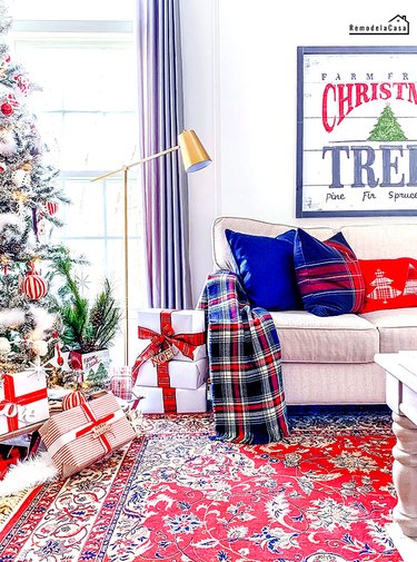 Living room with Christmas tree, artwork with the words Christmas tree, red rug, and red and blue pillows.