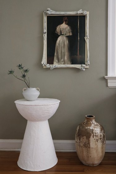 Moody portrait of woman in white gown framed with plastic bones hanging above a white side table and floor vase