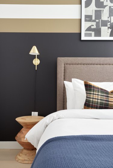 bedroom with black and tan walls, navy blanket and taupe headboard