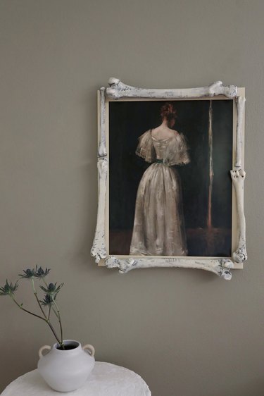 Moody portrait of woman in white gown framed with plastic bones hanging above a white table