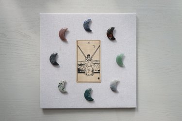 Moon-shaped crystals arranged in a circle around a tarot card on a linen backing board