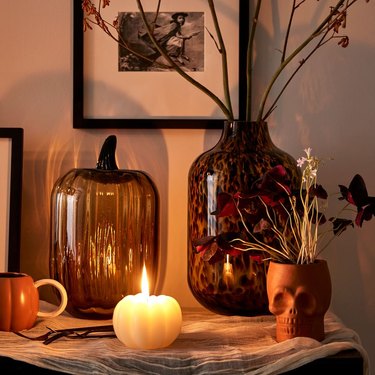 Glass pumpkins glowing orange next to an orange pumpkin candle and skull plants.